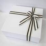 White gift box with a black and white striped ribbon on a light gray background